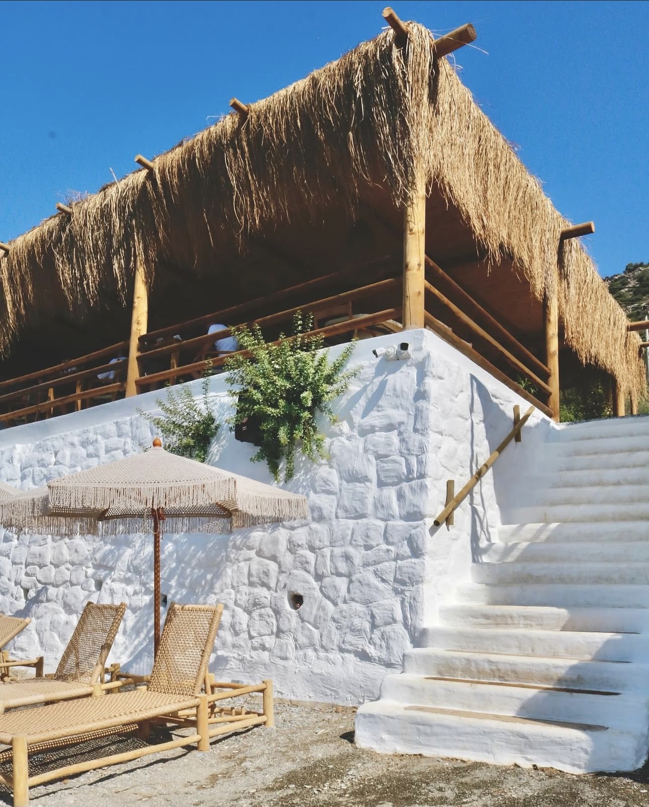 Mendelle Datça white stone walls under thatched roof, with sun beds and macramé umbrella